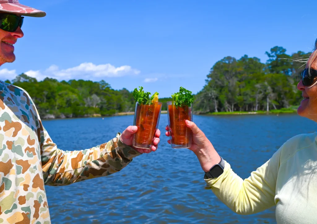 Two Bloody Marys raised in a toast over a scenic Carolina waterway