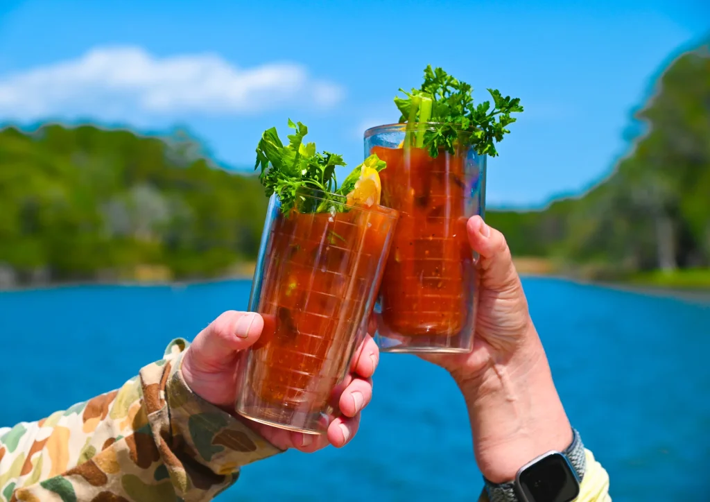 Two Bloody Marys held up in a celebratory toast by the water.