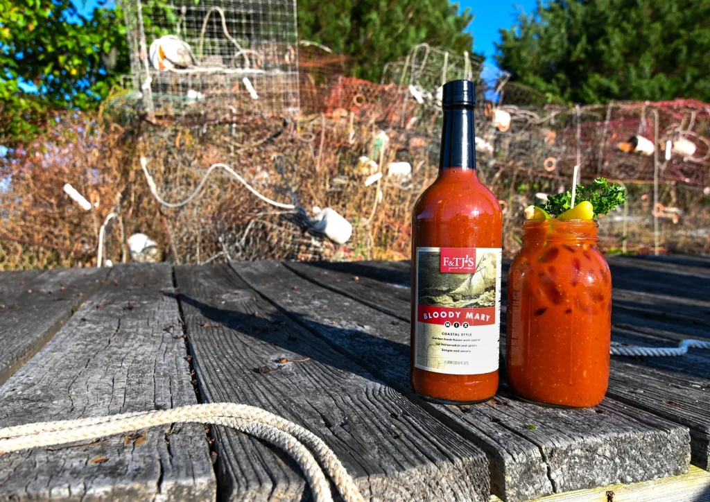 Close Up of F&TJ’s Bloody Mary Mix bottle resting alone on a dock beside a garnished drink