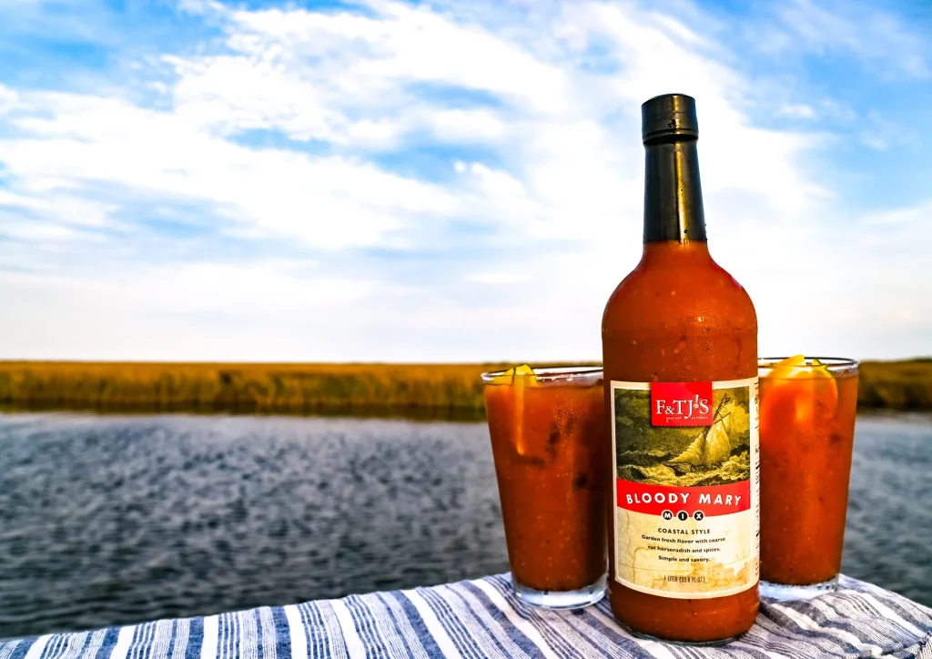 F&TJ’s Bloody Mary bottle and drink on a towel with a coastal Carolina water view.