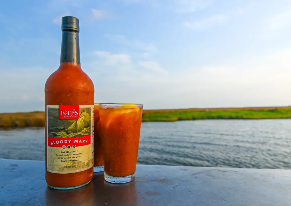 F&TJ’s Bloody Mary Mix bottle with a glass on a dock in coastal Carolina marsh