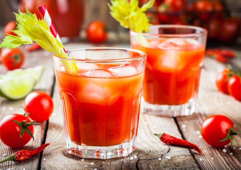 tomato juice with celery and ice in glasses on a wooden table